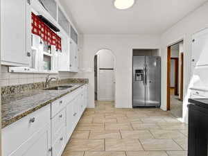Kitchen featuring stainless steel fridge, a sink, white cabinets, and stone countertops