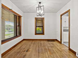 Unfurnished dining area with light wood finished floors, a chandelier, and baseboards