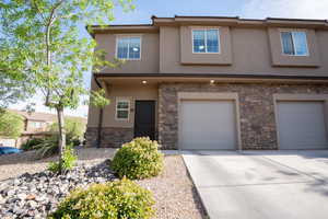 View of front facade featuring an attached garage, stucco siding, stone siding, and driveway