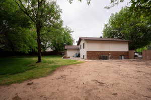 Rear view of property with a gate, fence, brick siding, central AC, and a lawn