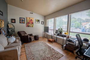 Office space featuring lofted ceiling, baseboards, visible vents, and light wood-style floors