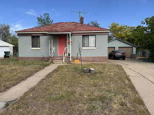 Bungalow with a front lawn, a garage, a chimney, concrete driveway, and an outdoor structure