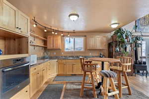 Kitchen featuring oven, a textured ceiling, light brown cabinetry, and light wood finished floors