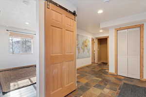 Hallway featuring baseboards, recessed lighting, a barn door, and stone finish floor