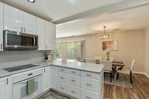 Kitchen with a peninsula, oven, white cabinets, stainless steel microwave, and black electric cooktop
