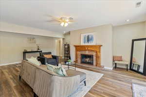 Living room with a ceiling fan, baseboards, a fireplace, and wood finished floors