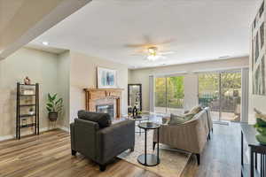 Living area with a tile fireplace, baseboards, wood finished floors, and a ceiling fan