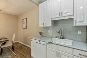 Kitchen with a sink, tasteful backsplash, dark wood-type flooring, dishwasher, and white cabinets