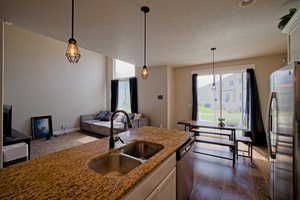 Kitchen featuring stone countertops, stainless steel appliances, a sink, and decorative light fixtures