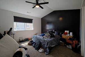 Carpeted bedroom featuring visible vents, lofted ceiling, and ceiling fan