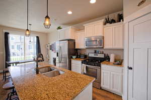 Kitchen with wood finished floors, a sink, stainless steel appliances, white cabinets, and a kitchen island with sink