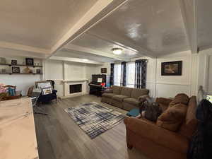 Living area with a fireplace with raised hearth, a textured ceiling, wood finished floors, and beam ceiling