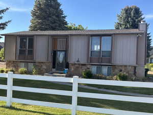 Raised ranch with a front lawn, a chimney, fence private yard, and stone siding