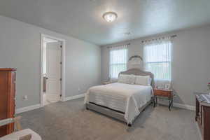 Bedroom with light carpet, visible vents, and a textured ceiling