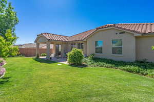 Back of house with a patio, a tiled roof, stucco siding, fence, and a lawn