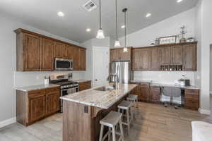 Kitchen featuring baseboards, visible vents, a sink, a kitchen bar, and appliances with stainless steel finishes