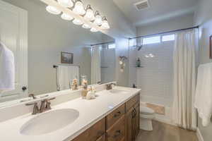 Bathroom with toilet, shower / bath combination with curtain, visible vents, and a sink