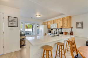 Kitchen featuring an updated  breakfast bar area, white appliances, a sink, a peninsula, and light countertops