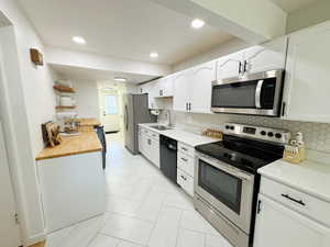 Kitchen featuring a sink, butcher block counters, backsplash, white cabinets, and appliances with stainless steel finishes