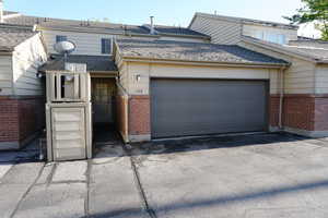 View of property featuring roof with shingles, a garage, brick siding, and driveway