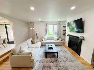 Living area featuring light wood-style flooring, arched walkways, a fireplace with flush hearth, and recessed lighting