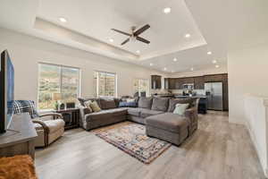 Living area with light wood-type flooring, recessed lighting, a ceiling fan, a raised ceiling, and baseboards
