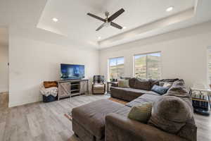 Living room featuring a ceiling fan, light wood-style flooring, recessed lighting, baseboards, and a raised ceiling