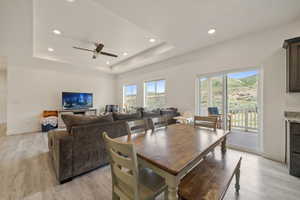 Dining space with a ceiling fan, baseboards, light wood finished floors, and a tray ceiling