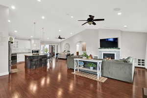 Living room with dark wood-type flooring, lofted ceiling, a ceiling fan, and a glass covered fireplace