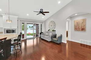 Living area featuring visible vents, ceiling fan, arched walkways, lofted ceiling, and dark wood-style floors