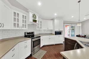 Kitchen featuring tasteful backsplash, light countertops, dark wood-style floors, glass insert cabinets, and appliances with stainless steel finishes