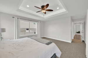 Carpeted bedroom with baseboards, a raised ceiling, recessed lighting, and a ceiling fan