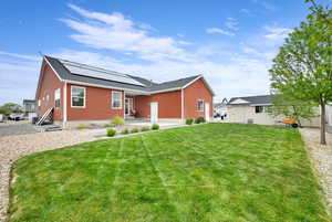 View of front of home with roof with shingles, a patio, entry steps, solar panels, and a front lawn