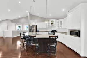 Kitchen with stainless steel appliances, dark wood finished floors, a sink, light countertops, and an island with sink