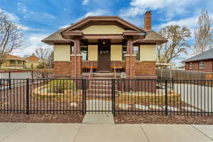 Bungalow-style home with brick siding, a porch, a chimney, and stucco siding