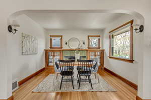Dining room with arched walkways, baseboards, visible vents, and wood finished floors