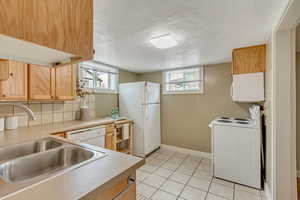 Kitchen featuring a sink, white appliances, decorative backsplash, light countertops, and light tile patterned floors