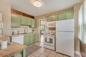 Kitchen with backsplash, green cabinetry, a sink, and white appliances