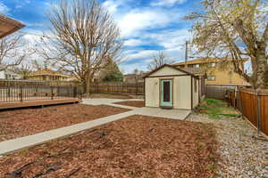 View of yard featuring a storage unit, a deck, a fenced backyard, an outbuilding, and a patio area