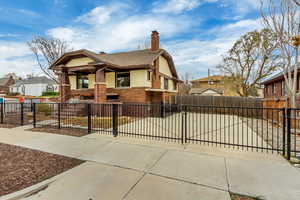 Bungalow-style home featuring roof with shingles, brick siding, a residential view, a fenced front yard, and a chimney