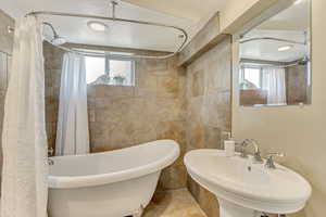 Full bath with tile walls, a healthy amount of sunlight, and a sink