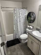 Full bath featuring toilet, shower / tub combo with curtain, stone finish flooring, and vanity