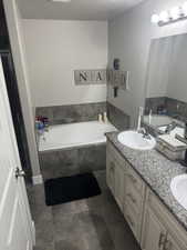 Full bathroom featuring a sink, double vanity, a textured ceiling, and a garden tub