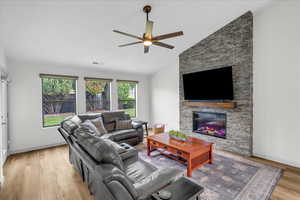 Living room featuring wood finished floors, a ceiling fan, visible vents, a stone fireplace, and vaulted ceiling