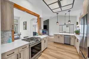 Kitchen with a peninsula, light brown cabinetry, a fireplace, light countertops, and appliances with stainless steel finishes
