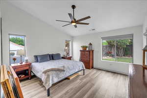 Bedroom featuring vaulted ceiling, multiple windows, visible vents, and light wood-style floors