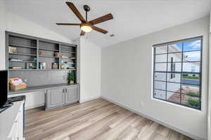 Interior space featuring built in desk, light wood-style flooring, lofted ceiling, and ceiling fan