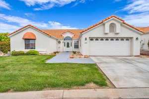 Mediterranean / spanish home featuring driveway, a tiled roof, a garage, stucco siding, and a front lawn