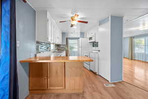 Kitchen featuring a peninsula, white appliances, light wood-style flooring, and tasteful backsplash