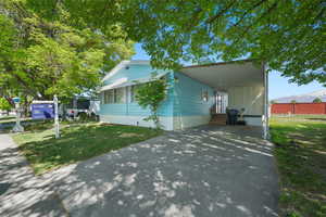 Manufactured / mobile home with concrete driveway, entry steps, an attached carport, and a front lawn